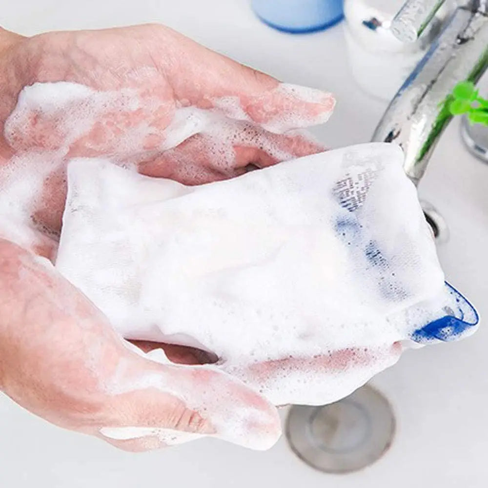 Hands are squeezing a white exfoliating mesh soap pouch onto a showerhead for cleaning.