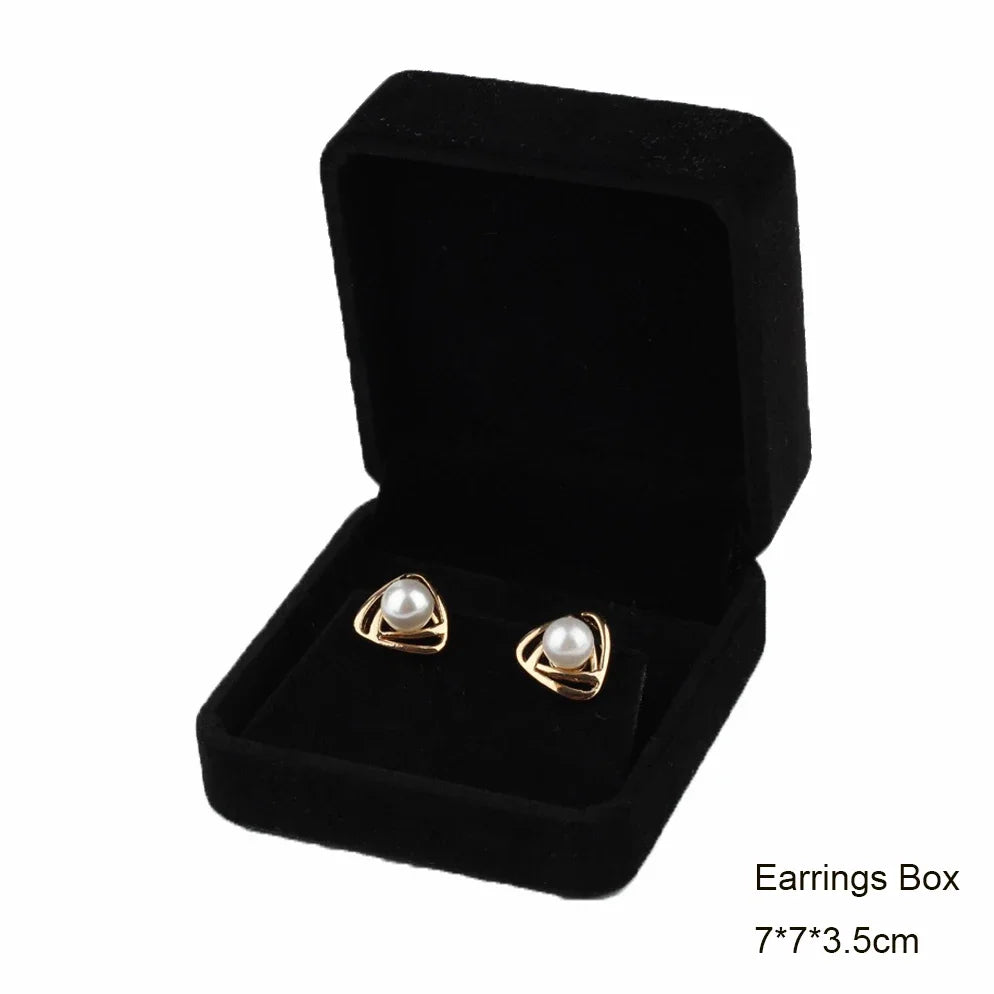 Black velvet jewelry storage box set with a gold-toned pair of earrings inside