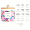 A clear glass container filled with colorful laundry pods and a lid, displayed next to various laundry accessories.