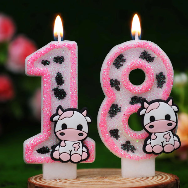 Two pink candles shaped like the numbers 1 and 8 with black cow print designs for birthday decor