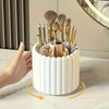 A white cylindrical organizer holding various gold and brown makeup brushes and tools.