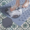 Los pies de una persona se remojan en una estera de masaje gris antideslizante sobre un suelo de azulejos estampados.
