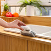 A hand is placing a gray cleaning brush into a white sink basin for cleaning.