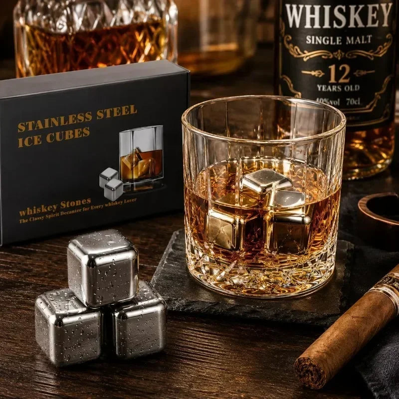 A glass of whiskey with stainless steel ice cubes on a dark wooden surface next to a whiskey bottle and ice cubes.