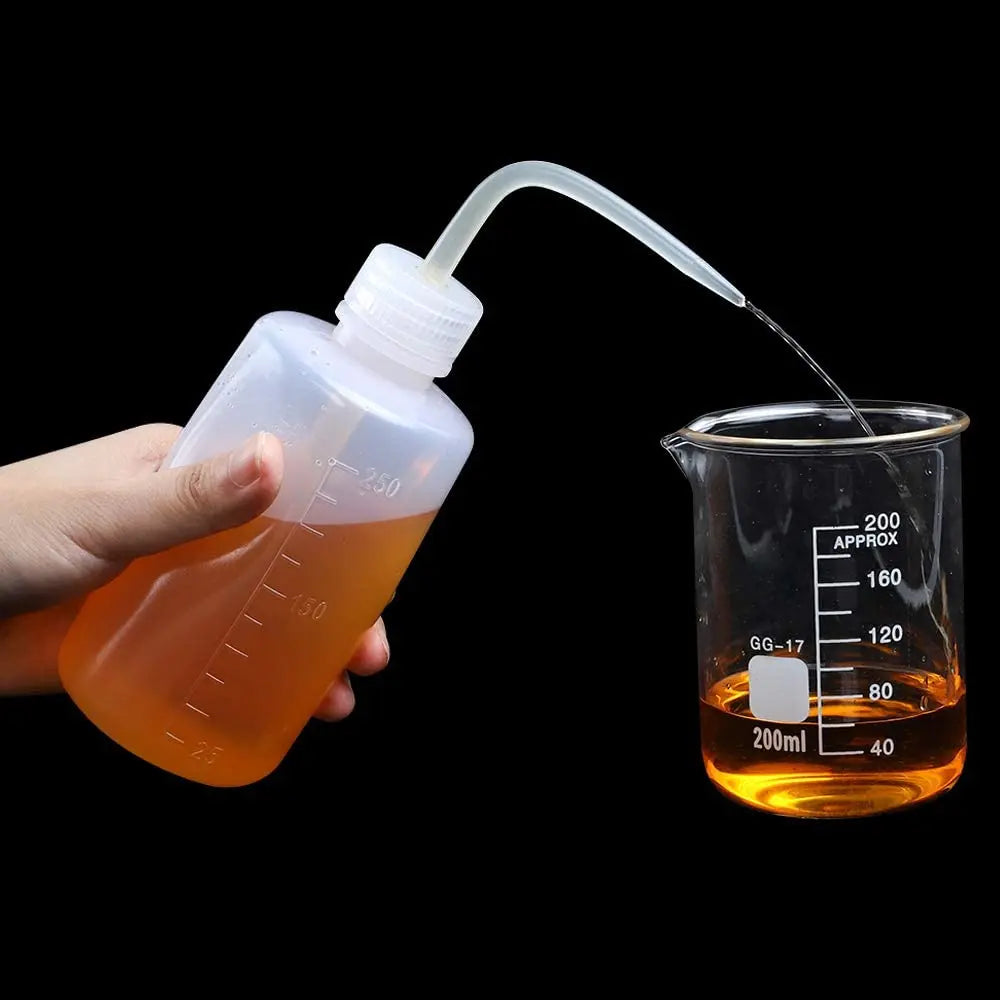 A hand is squeezing an amber liquid from a plastic bottle into a glass measuring cup for tattoo solutions.
