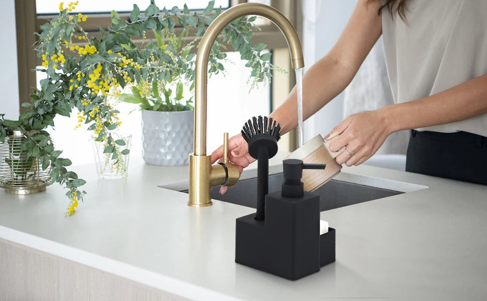 A hand is operating a brass kitchen faucet with a sponge holder and brush accessory on a white countertop.