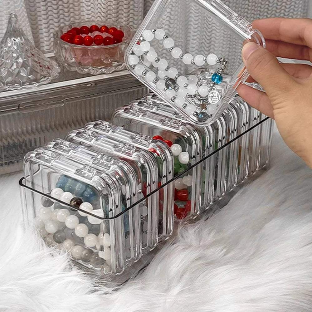 A hand is holding a clear plastic jewelry organizer box filled with various beads and jewelry.