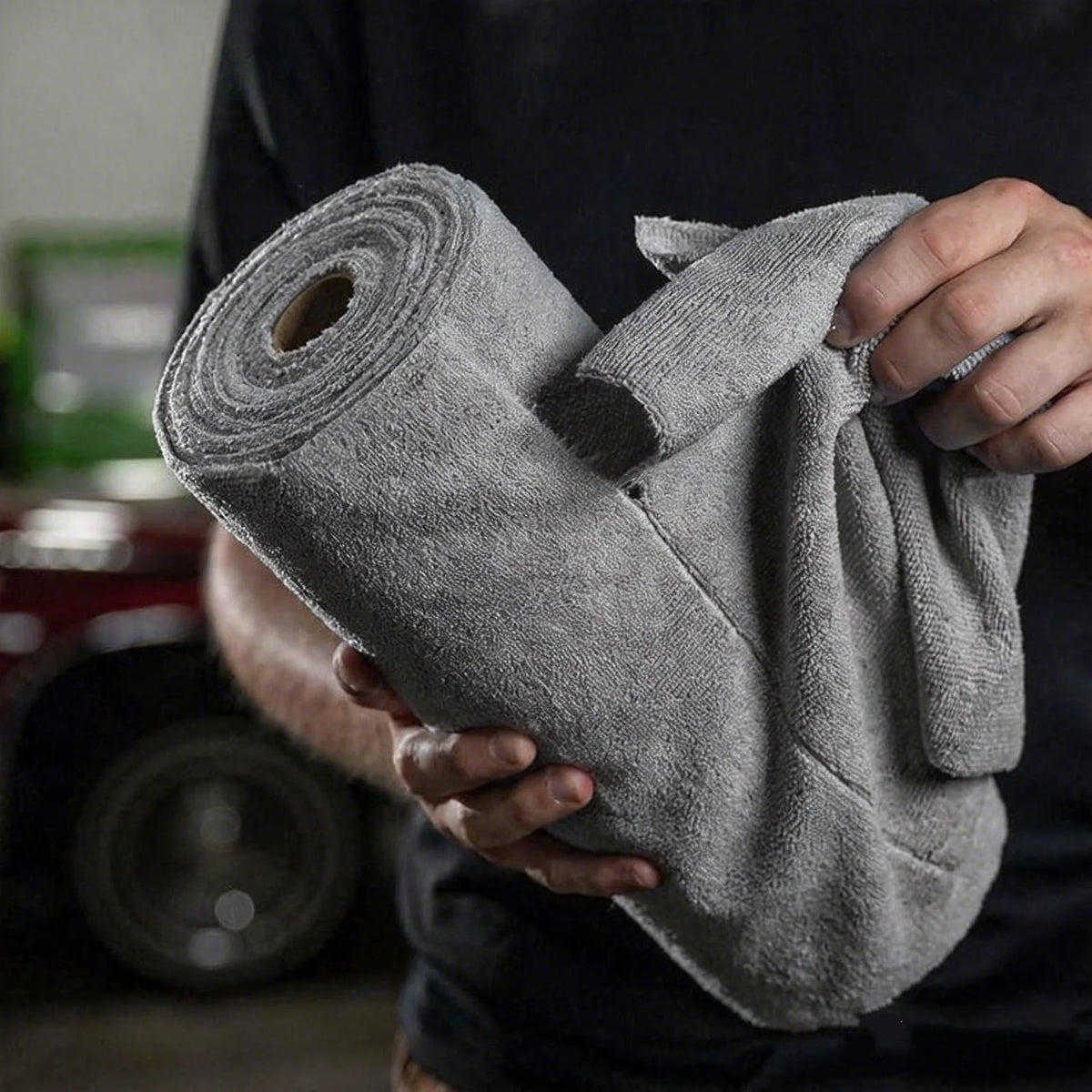 A hand holds a roll of gray tearable microfiber cleaning wipes.