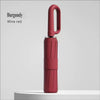 A burgundy wine red large automatic folding umbrella standing upright on a white surface.