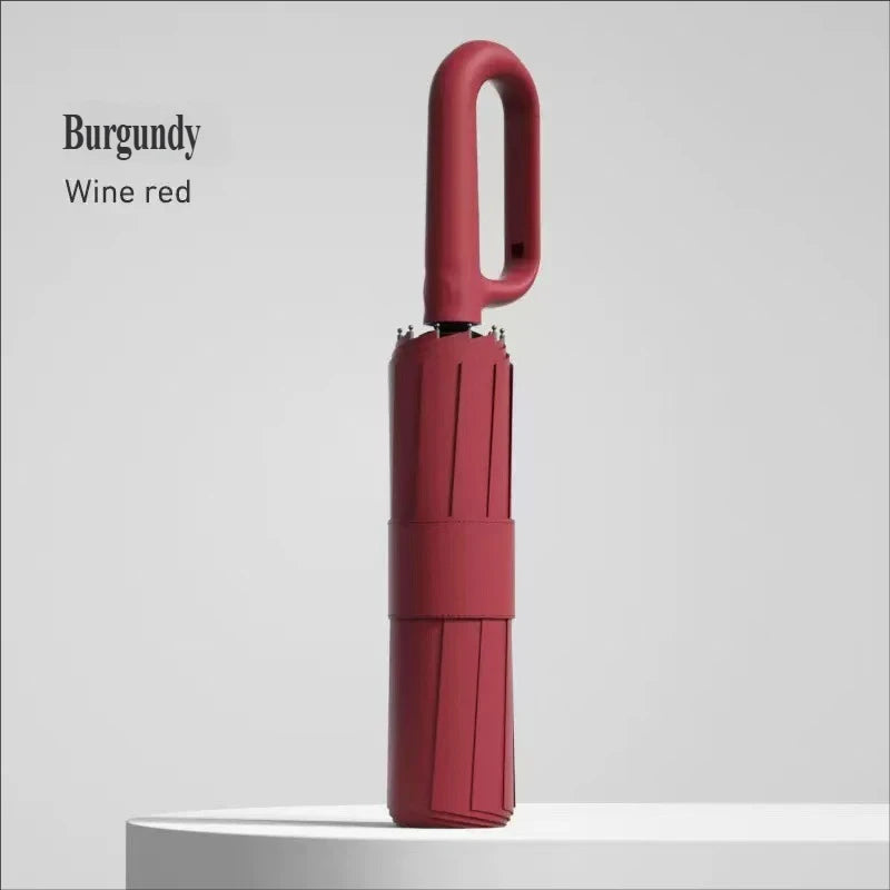A burgundy wine red large automatic folding umbrella standing upright on a white surface.