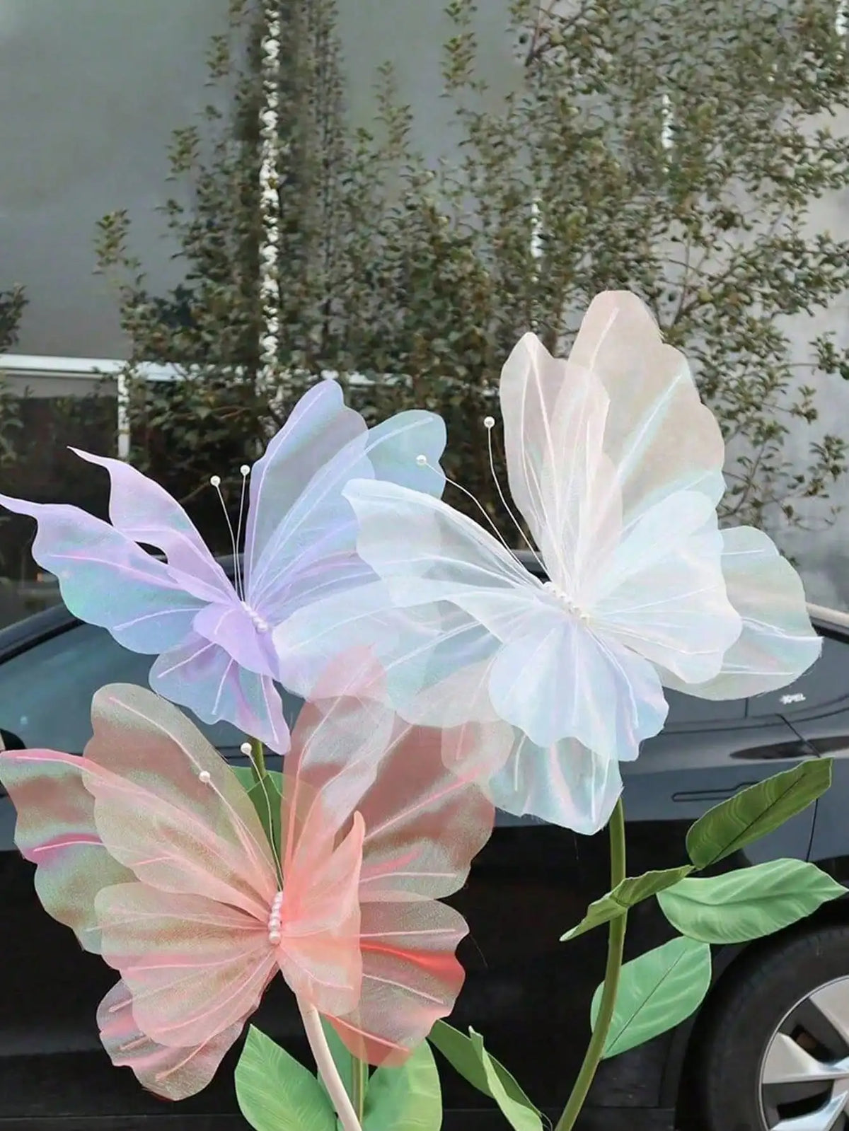 A cluster of pink, purple, and white 3D simulated butterfly decorations on a green plant stem.