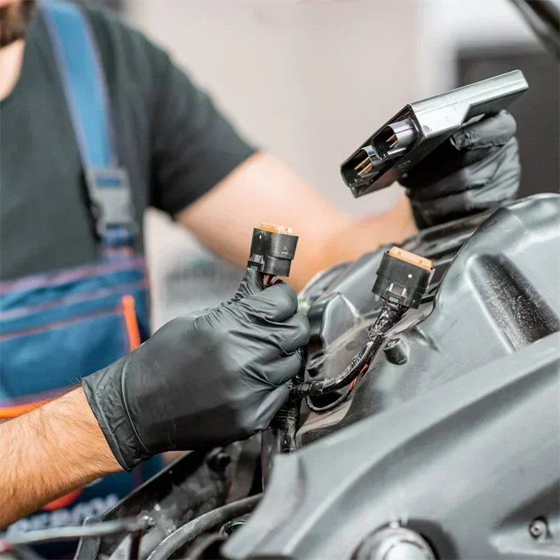 A person wearing black nitrile gloves is using a tool to work on a car engine component.