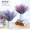 A bouquet of purple and lavender artificial flowers in a white vase displayed on a wooden table.