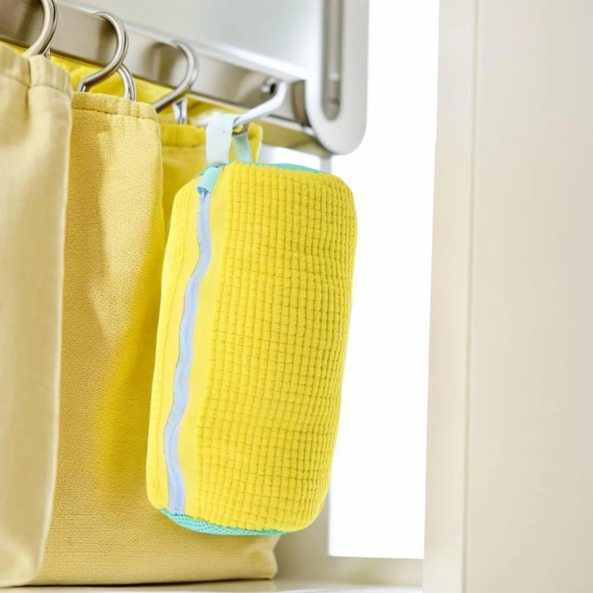 A bright yellow reusable shoe washing bag with a light blue stripe hanging on a rack.