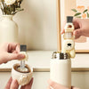 Hands are shown using a white silicone brush set to clean a white metal bottle and cup.