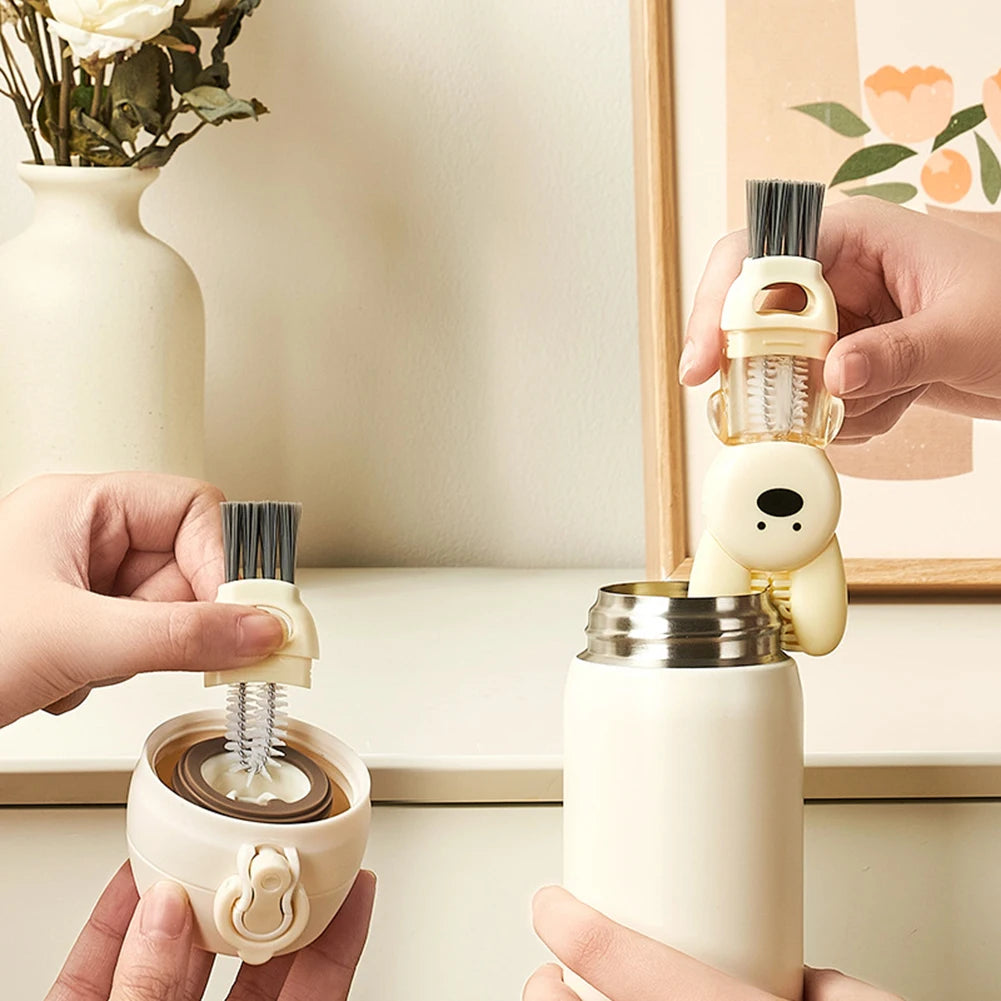 Hands are shown using a white silicone brush set to clean a white metal bottle and cup.