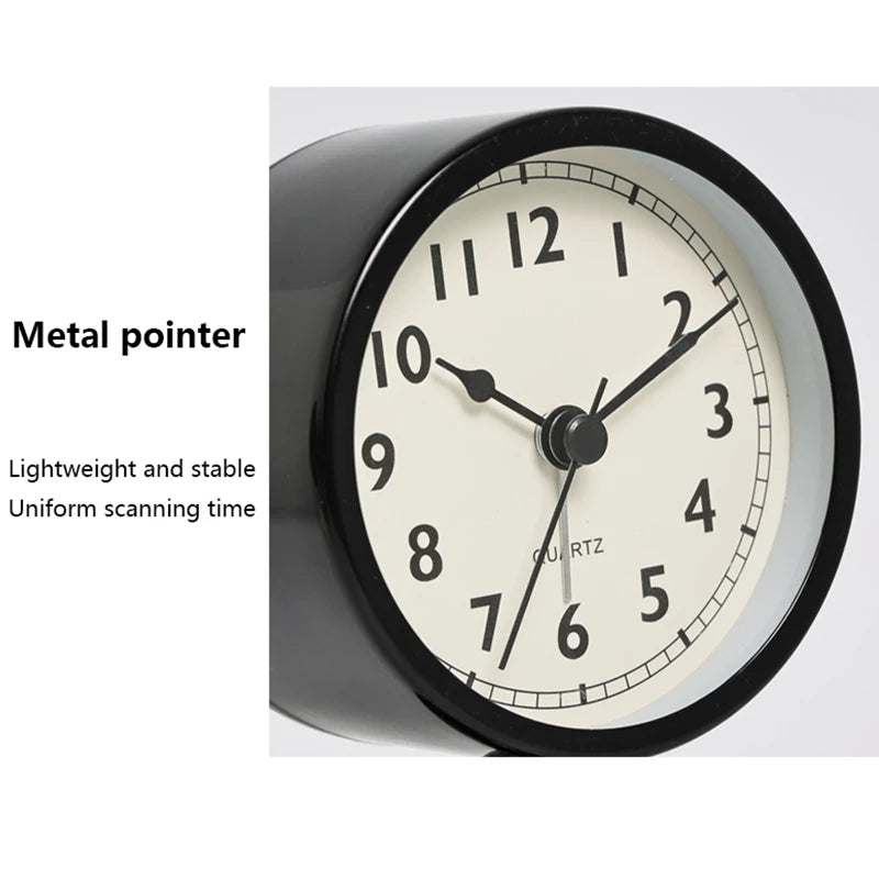 A close-up view of a black round alarm clock with a metal pointer and a light-colored face.