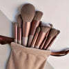 A set of luxury vegan makeup brushes in various shades of rose gold and nude stored in a beige pouch.