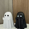 A white ghost statue and a black ghost statue are displayed against a wooden background.