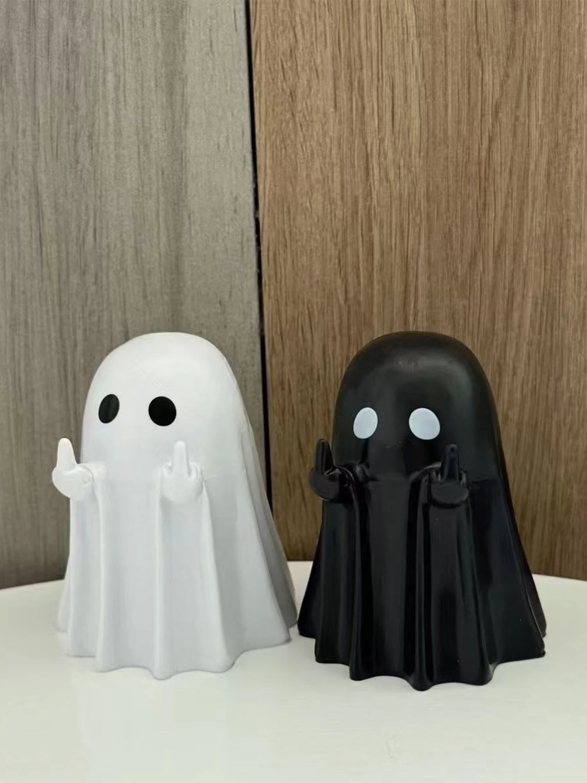 A white ghost statue and a black ghost statue are displayed against a wooden background.