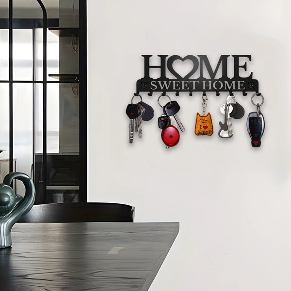 A black metal wall key holder rack with the words HOME SWEET HOME mounted on a white wall.