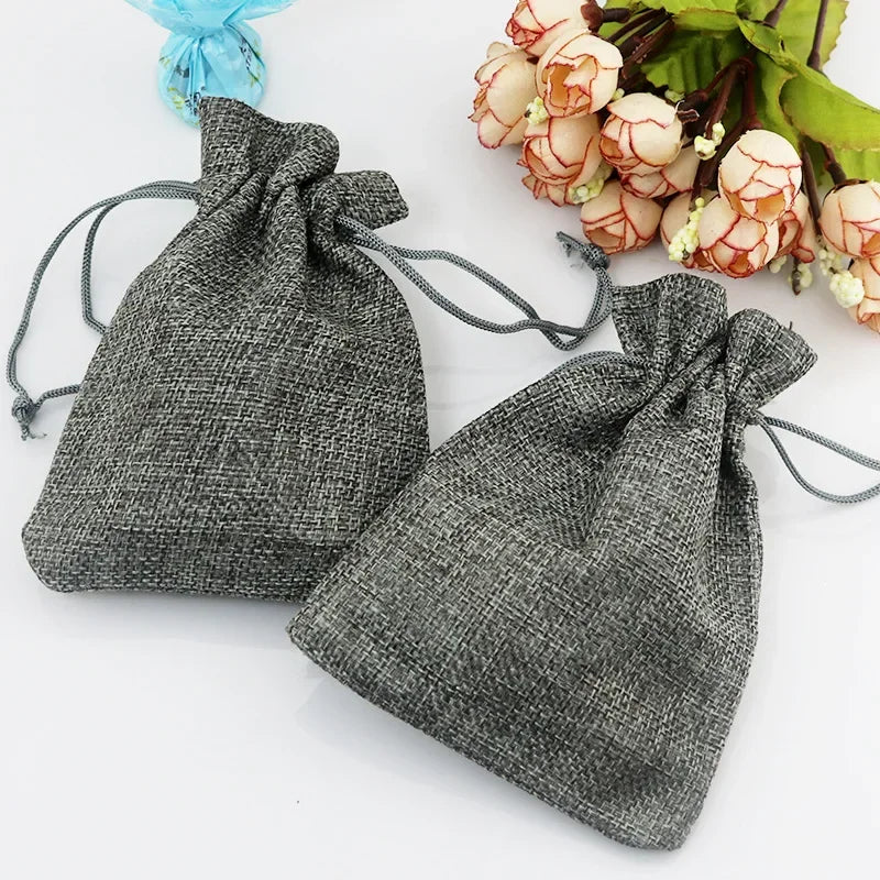 Zwei graue Jute- und Leinen-Geschenktüten mit hellrosa floralen Akzenten werden auf weißem Hintergrund präsentiert.