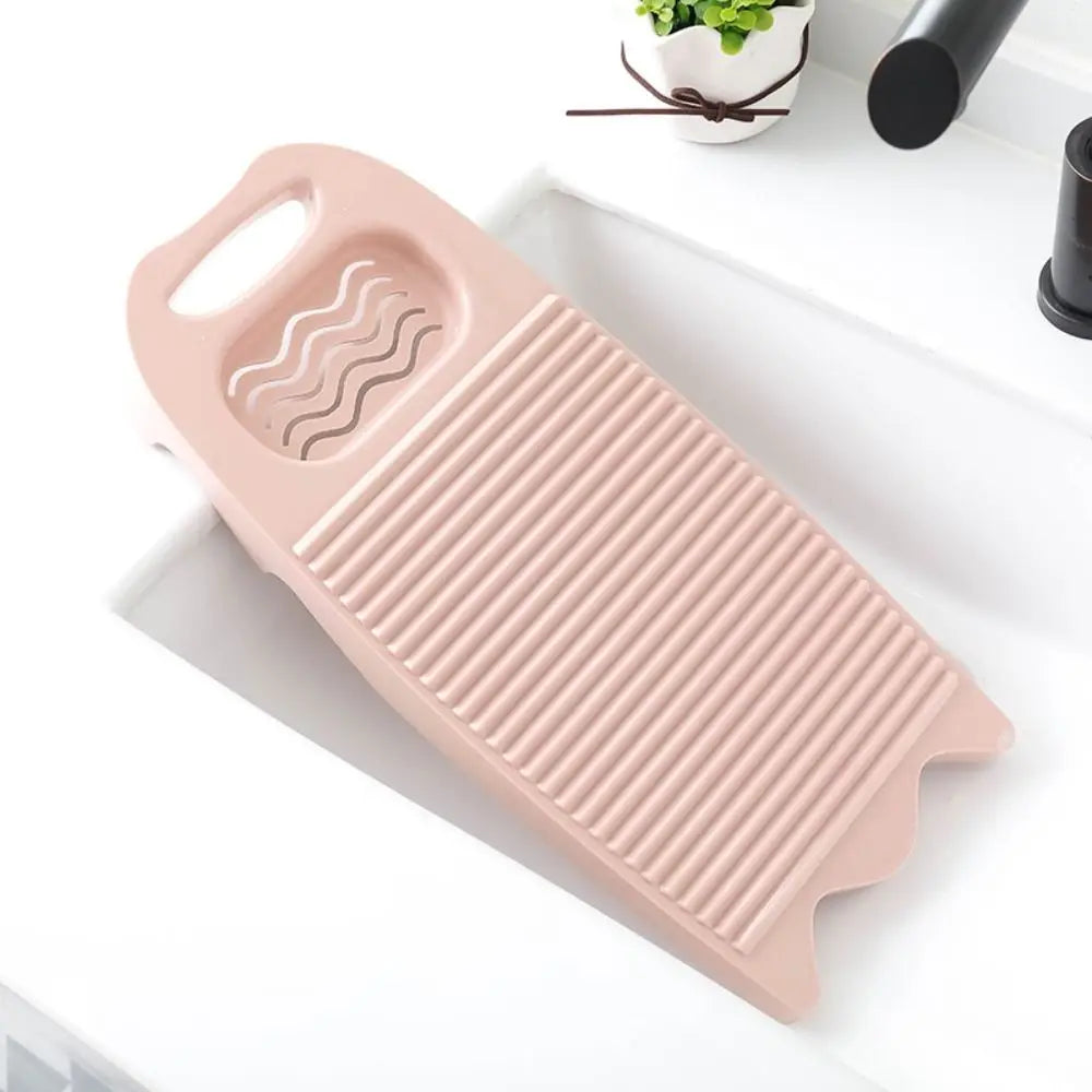 A pink durable plastic washing board with ridges and a handle is shown on a white surface.