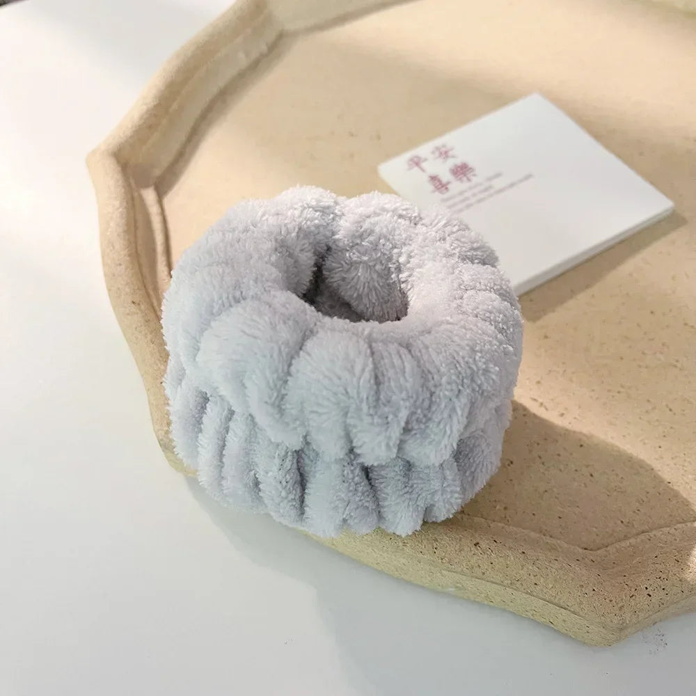 A light gray microfiber wrist sweatband set resting on a beige tray next to a white card.
