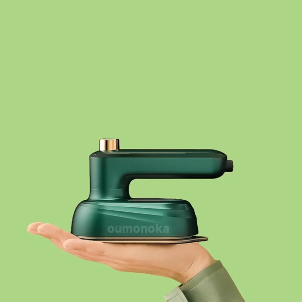 A hand holds a small, dark green mini rotating handheld garment steamer against a light green background.