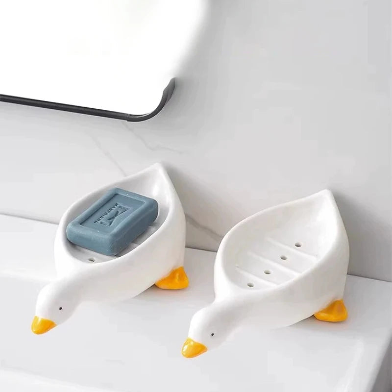 White duck-shaped soap dish with a yellow beak sitting on a white bathroom counter.