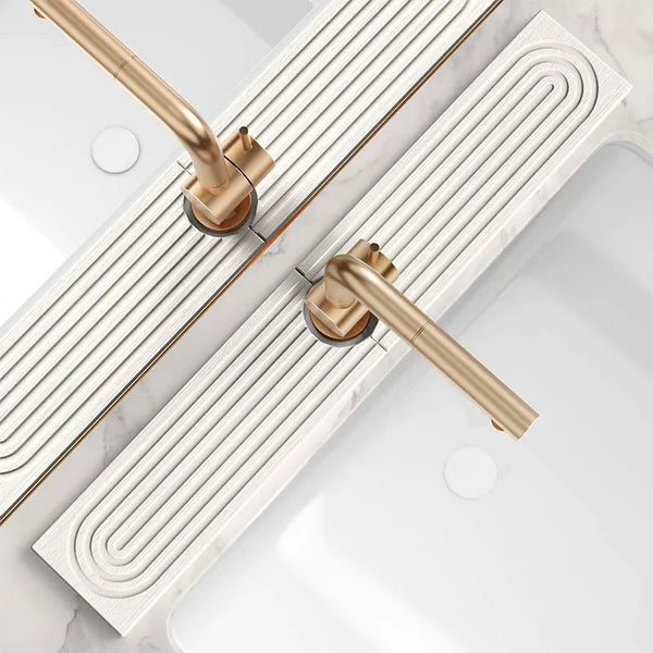 A gold-toned faucet and drain assembly installed on a white marble countertop, featuring a modern linear splash guard mat.