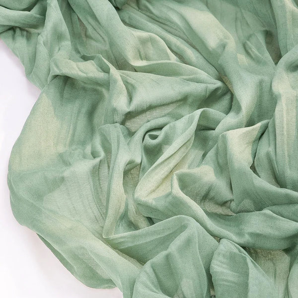 A close-up of a flowing, sheer sage green fabric used as a boho table runner.