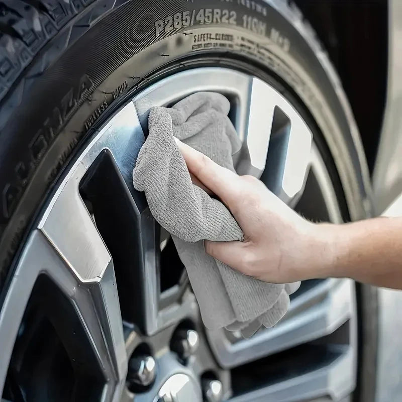 A hand is wiping a car wheel with a gray reusable microfiber cleaning cloth.