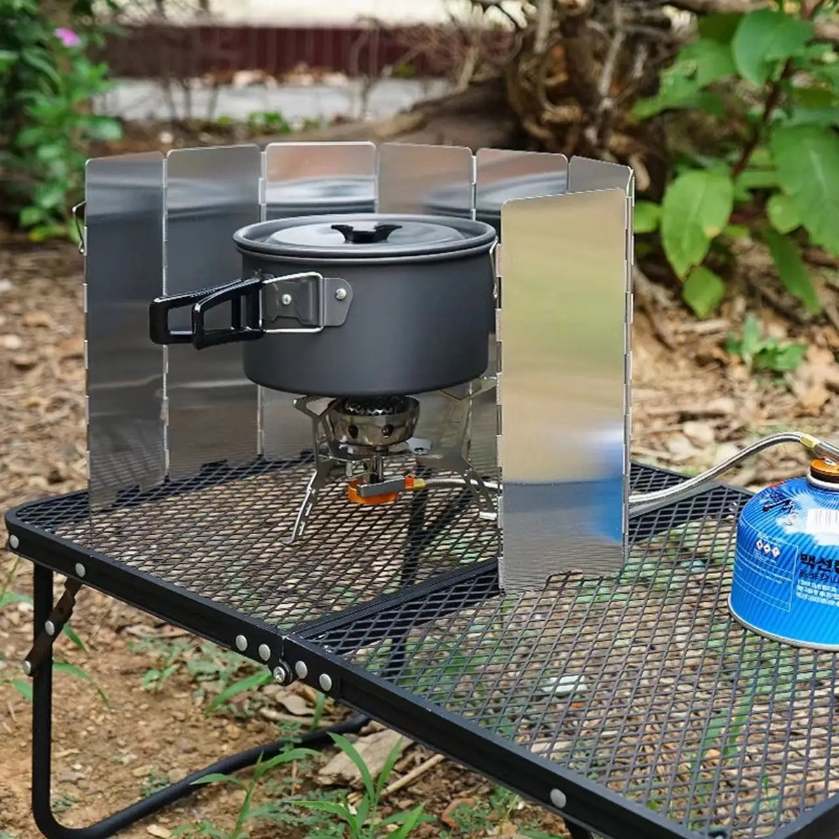 A multi-plate outdoor gas stove with a wind shield mounted on a black metal grate.