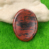 A polished, reddish-brown natural quartz thumb stone resting on vibrant green grass.