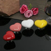 A collection of heart-shaped toilet presser buttons in shades of pink, red, and yellow are displayed on a dark surface.