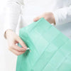 A hand is holding a green disposable toilet seat cover, showing its texture and fold.
