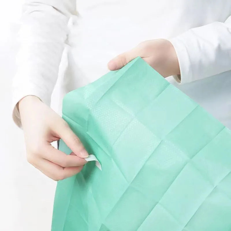 A hand is holding a green disposable toilet seat cover, showing its texture and fold.
