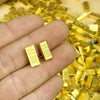A hand holds several small gold bar decorative ornaments against a background of loose gold bars.