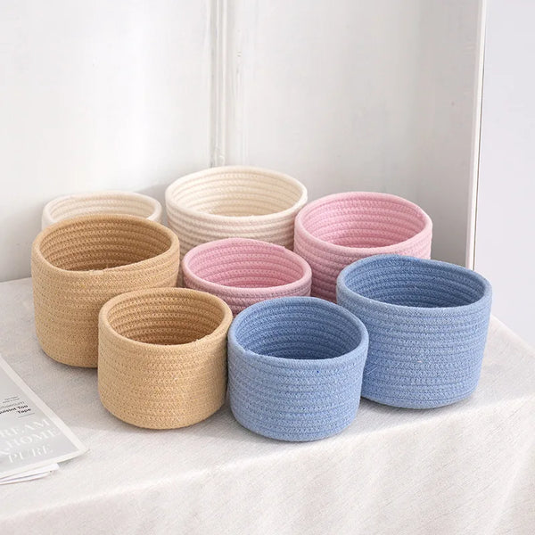 A collection of handwoven cotton rope storage baskets in various natural and pastel shades are displayed on a white surface.