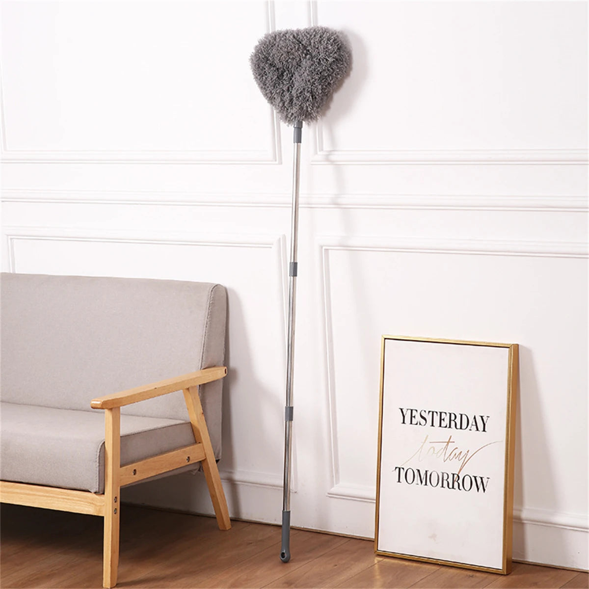 A silver extendable ceiling fan duster with a fluffy gray brush hanging on a white wall.