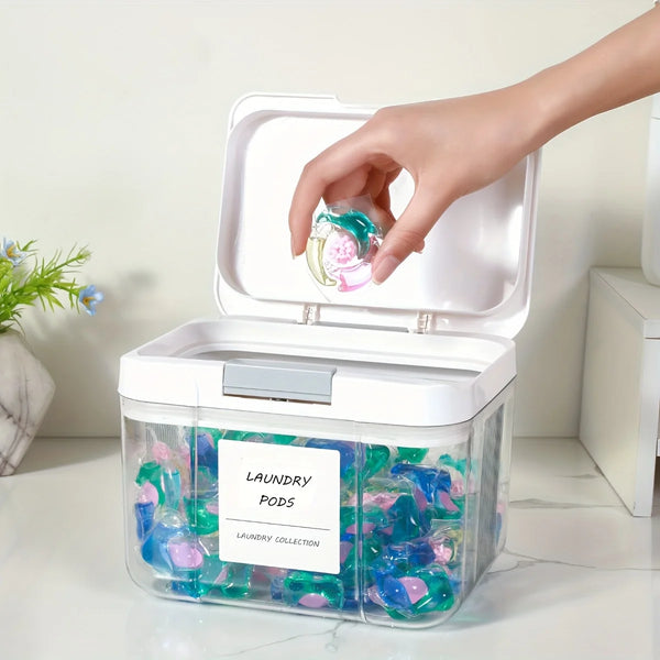 A hand is opening a clear plastic laundry pod organizer with a white lid, revealing colorful laundry pods inside.