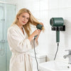 Une femme blonde utilise un support de sèche-cheveux mural dans une salle de bain moderne pour sécher ses cheveux.