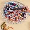 A glass dish filled with a colorful assortment of tiny beads and stringing materials for crafting and decoration
