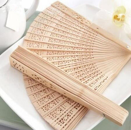 Un éventail pliable en bois clair avec des motifs complexes est exposé sur une assiette blanche.