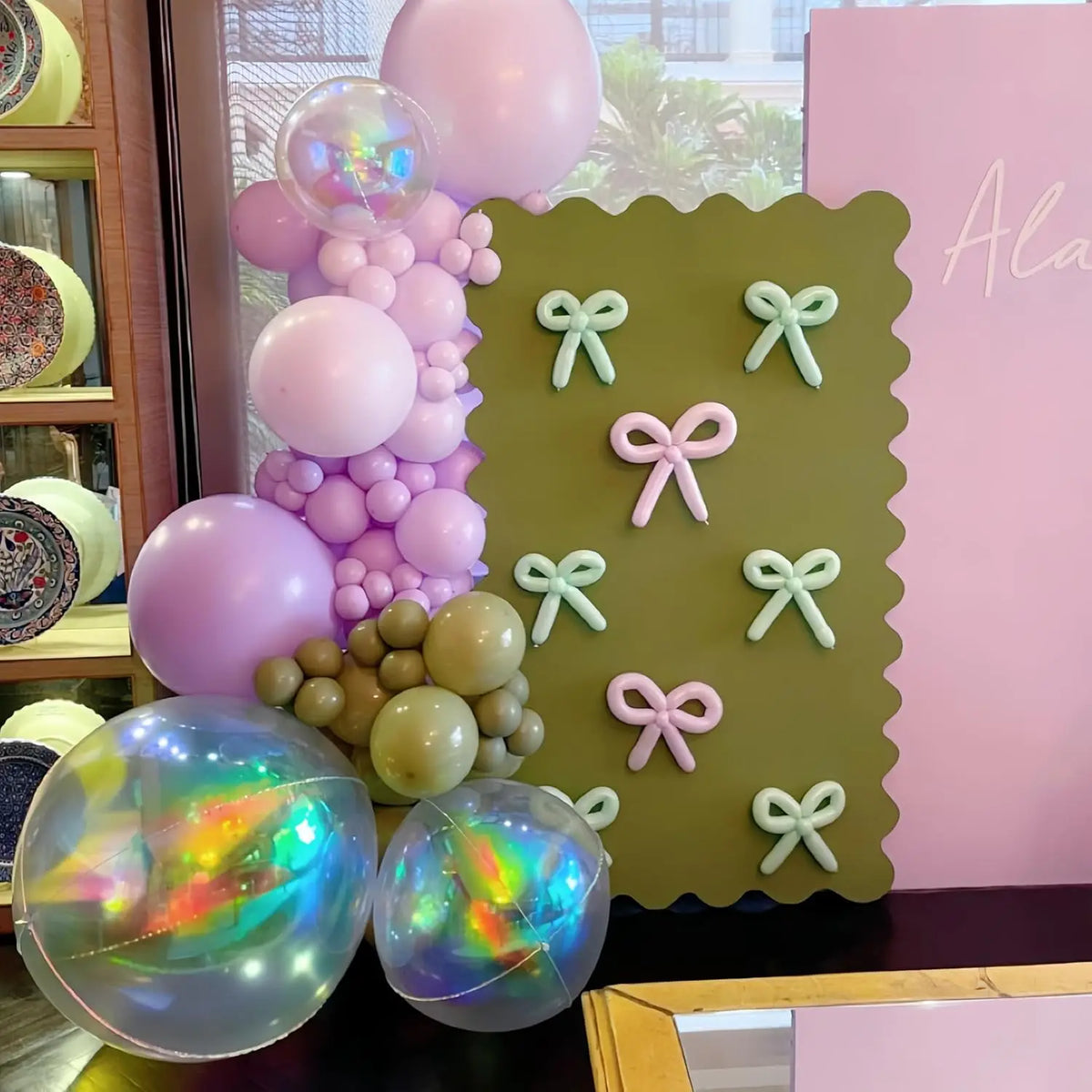 Eine Sammlung irisierender holografischer Partyballons in Rosa- und Violetttönen vor rosa Hintergrund.