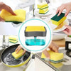 A hand is using a dual-function liquid soap dispenser with a sponge holder to wash dishes.