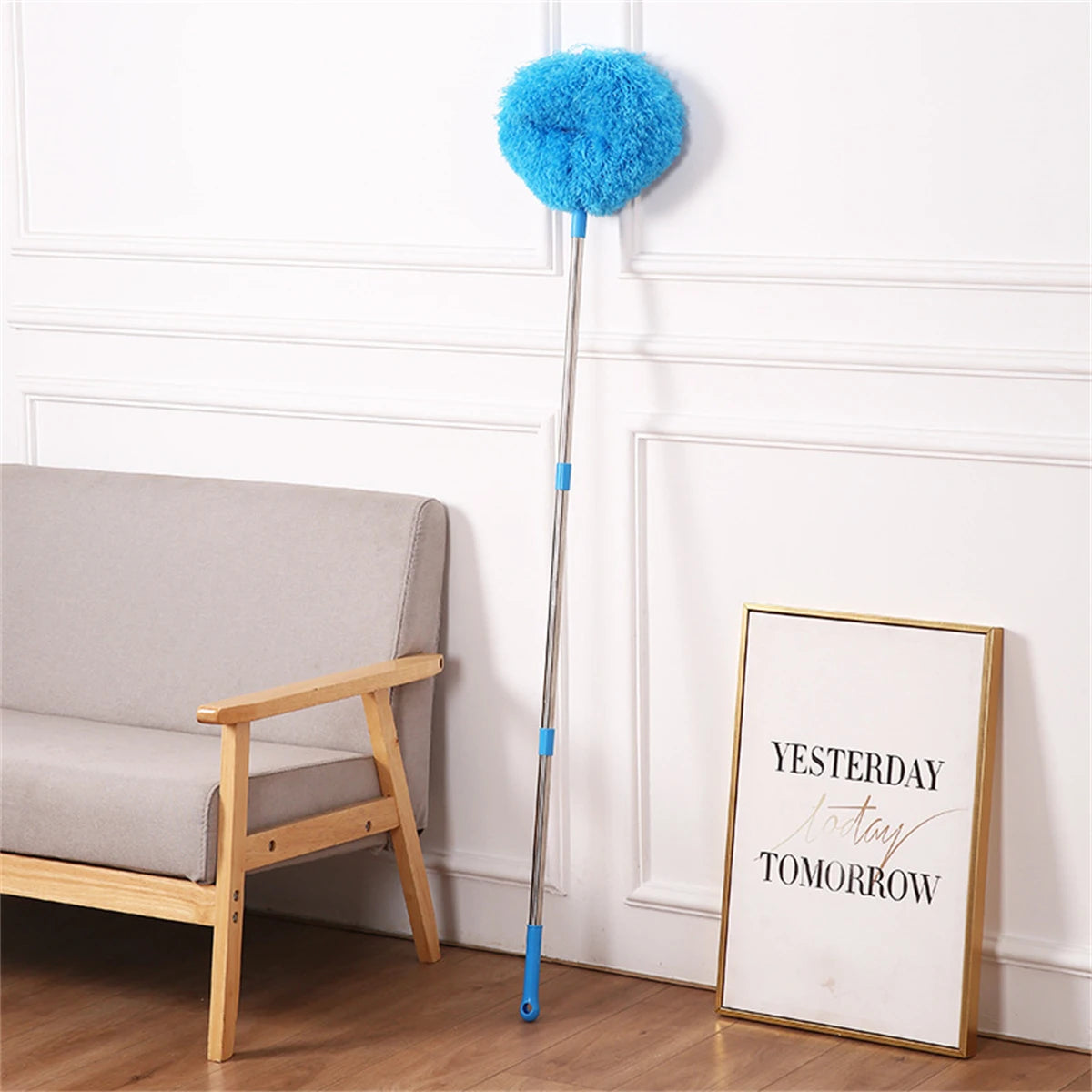 A blue fuzzy duster attached to a long pole is displayed next to a wooden chair and a framed sign.