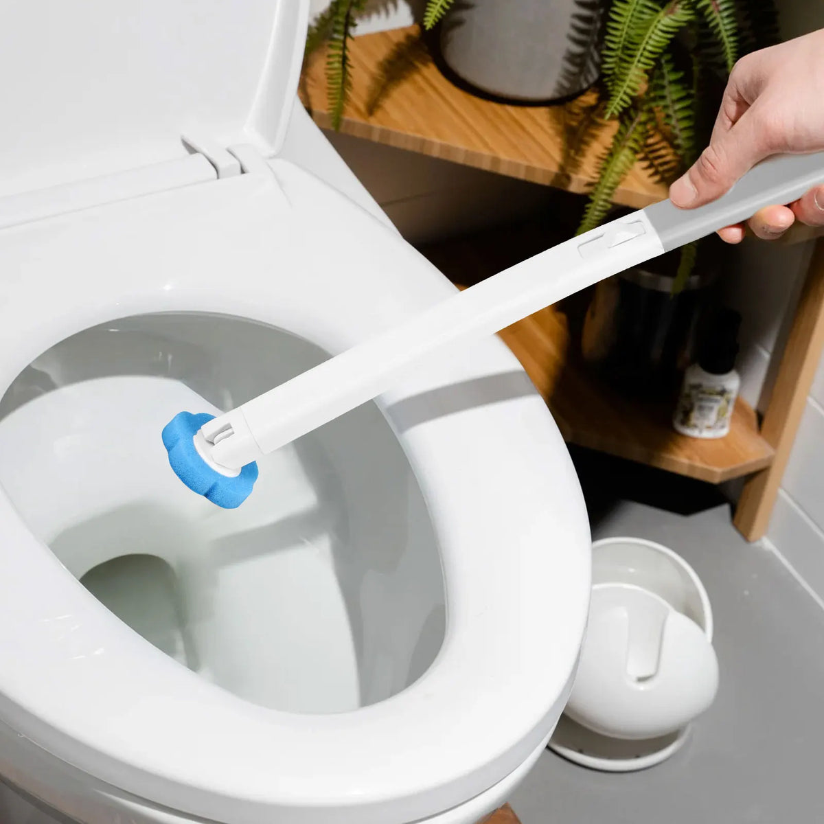 Une main utilise une brosse à toilette jetable blanche pour nettoyer l'intérieur d'une cuvette de toilette blanche.