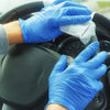 A hand wearing a blue nitrile disposable glove is wiping down a car interior surface.